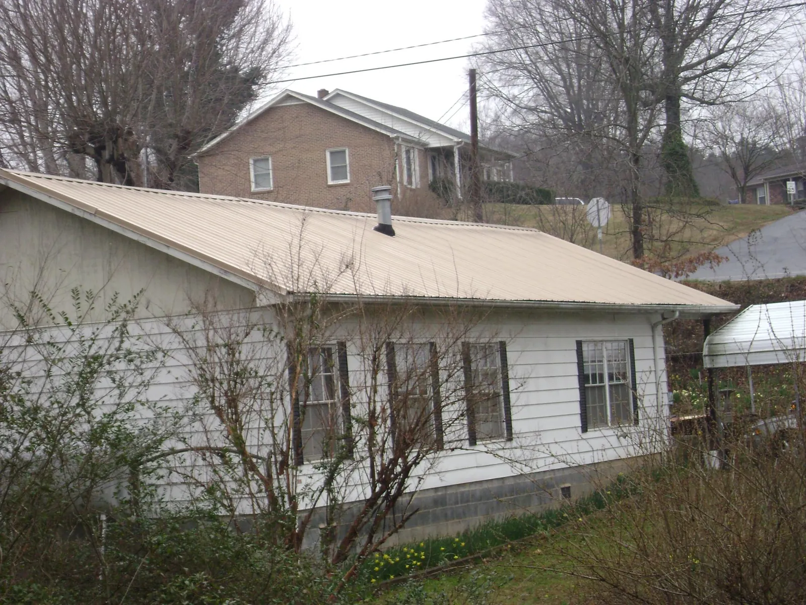 Tan metal roof on a white sided house set into a hillside — Commercial Roofing by Roofing Brothers in Sea Isle City